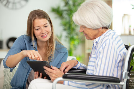 Individuelle Pflegeberatung bei PflegeBetreuer – persönlich und digital | © PflegeBetreuer | unabhängige Pflegeberatung Junge Frau berät Seniorin im Rollstuhl mithilfe eines Tablets – Pflegeberatung zu Hause | © PflegeBetreuer | unabhängige Pflegeberatung